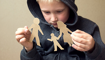 A young boy, looking disappointed, holds paper cutouts of a family